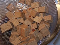 Den fertig marinierten Tofu über einem Sieb abgießen. Es ist deutlich zu sehen, wie stark der Tofu die Marinade aufgenommen hat.