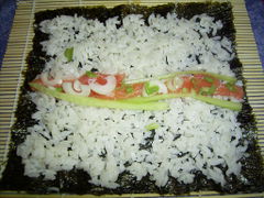 Die Zutaten in einem schmalen Streifen auf dem Reis verteilen und mit Wasabi bestreichen.